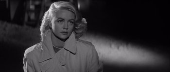 Movie still from “The Tarnished Angels” (1957), directed by Douglas Sirk – A black and white photo of a woman in a trench coat; Close Up shot, Low angle