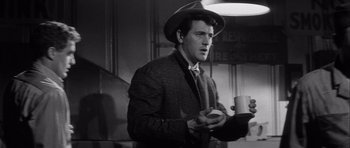 Movie still from “The Tarnished Angels” (1957), directed by Douglas Sirk – A black and white photo of a man holding a coffee cup; Medium shot, Low angle