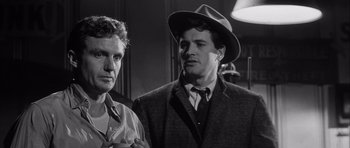 Movie still from “The Tarnished Angels” (1957), directed by Douglas Sirk – A man in a hat standing next to another man in a suit; Close Up shot, Low angle