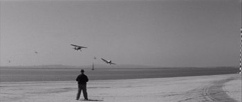 Movie still from “The Tarnished Angels” (1957), directed by Douglas Sirk – A man standing on a beach watching planes fly in the sky; Extreme Wide shot, Low angle