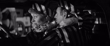 Movie still from “The Tarnished Angels” (1957), directed by Douglas Sirk – A man and a woman are standing under a striped umbrella; Medium shot, High angle