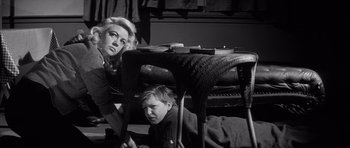 Movie still from “The Tarnished Angels” (1957), directed by Douglas Sirk – A woman and a boy sitting under a chair; Medium shot, Low angle