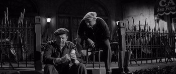 Movie still from “The Tarnished Angels” (1957), directed by Douglas Sirk – Two men are sitting on a chair and one is holding a beer; Medium shot, High angle