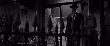 Movie still from “The Tarnished Angels” (1957), directed by Douglas Sirk – A black and white photo of a man in a suit and hat; Wide shot, Low angle