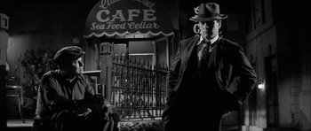 Movie still from “The Tarnished Angels” (1957), directed by Douglas Sirk – A black and white photo of a man in a suit and a hat; Medium shot, Low angle