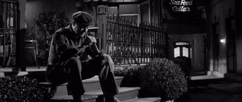 Movie still from “The Tarnished Angels” (1957), directed by Douglas Sirk – A black and white photo of a man sitting on steps; Medium shot, Low angle