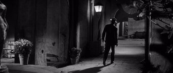 Movie still from “The Tarnished Angels” (1957), directed by Douglas Sirk – A man wearing a hat standing next to a lamp post; Wide shot, Low angle