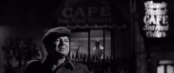 Movie still from “The Tarnished Angels” (1957), directed by Douglas Sirk – A black and white photo of a man in front of a cafe; Medium shot, Low angle