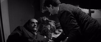 Movie still from “The Tarnished Angels” (1957), directed by Douglas Sirk – A man is smoking a cigarette while another man is sitting down; Medium shot, High angle