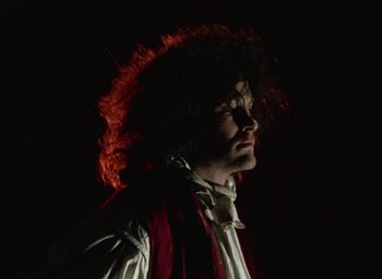 Movie still from “The Tempest” (1979), directed by Derek Jarman – A man with red hair is standing in the dark; Close Up shot, Low angle