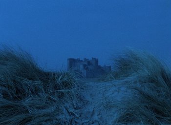 Movie still from “The Tempest” (1979), directed by Derek Jarman – A view of a castle from the beach at night; Extreme Wide shot, Low angle