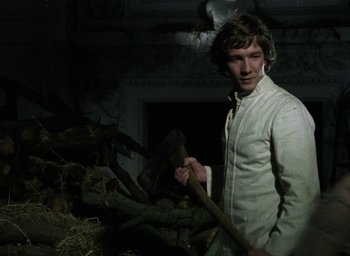 Movie still from “The Tempest” (1979), directed by Derek Jarman – A man holding an axe standing next to a pile of wood; Medium shot, Low angle