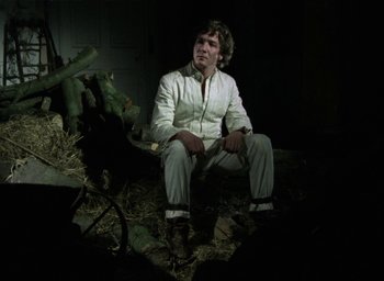 Movie still from “The Tempest” (1979), directed by Derek Jarman – A man sitting on a pile of hay in the dark; Medium shot, Low angle