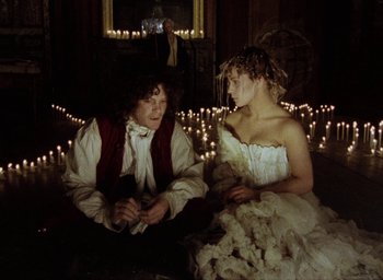 Movie still from “The Tempest” (1979), directed by Derek Jarman – A man and a woman sitting in front of candles; Medium shot, High angle