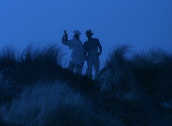 Movie still from “The Tempest” (1979), directed by Derek Jarman – Two men standing on top of a hill at night; Extreme Wide shot, Low angle