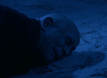 Movie still from “The Tempest” (1979), directed by Derek Jarman – An old man laying on the ground in the dark; Close Up shot, High angle
