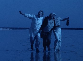 Movie still from “The Tempest” (1979), directed by Derek Jarman – A group of people running on the beach at night; Wide shot, High angle