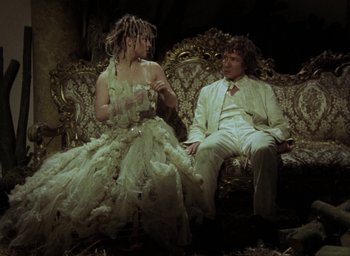 Movie still from “The Tempest” (1979), directed by Derek Jarman – A man and a woman sitting on a couch in front of each other; Medium shot, Low angle