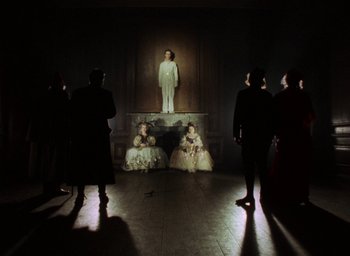 Movie still from “The Tempest” (1979), directed by Derek Jarman – A group of people standing in a dark room; Wide shot, Low angle
