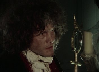 Movie still from “The Tempest” (1979), directed by Derek Jarman – A man with curly black hair and a white shirt; Close Up shot, Over the shoulder angle