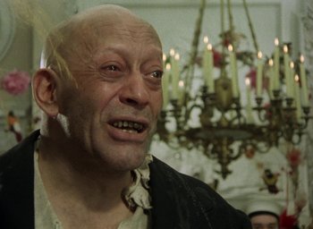 Movie still from “The Tempest” (1979), directed by Derek Jarman – An old man in a black shirt and a chandelier in the background; Close Up shot, Low angle