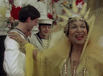 Movie still from “The Tempest” (1979), directed by Derek Jarman – An older woman in a yellow dress and a man in a white suit; Close Up shot, Over the shoulder angle
