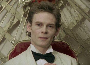 Movie still from “The Tempest” (1979), directed by Derek Jarman – A man in a bow tie holding an open umbrella; Close Up shot, Low angle