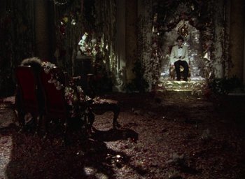 Movie still from “The Tempest” (1979), directed by Derek Jarman – A man sitting on a chair in a room with flowers; Extreme Wide shot, High angle