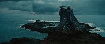 Movie still from “The Tempest” (2010), directed by Julie Taymor – A person in a costume standing on a rock by the ocean; Wide shot, Low angle