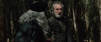Movie still from “The Tempest” (2010), directed by Julie Taymor – A man in a black and gold jacket standing next to an old man; Medium shot, Over the shoulder angle