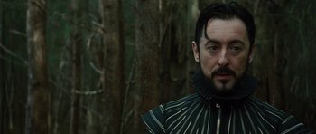 Movie still from “The Tempest” (2010), directed by Julie Taymor – A person wearing a costume near a forest; Close Up shot, Over the shoulder angle