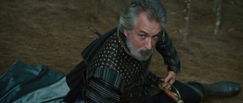 Movie still from “The Tempest” (2010), directed by Julie Taymor – An older man with a beard wearing a black and gold outfit; Close Up shot, High angle