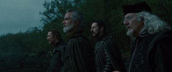 Movie still from “The Tempest” (2010), directed by Julie Taymor – A group of men standing next to each other in a wooded area; Medium shot, Low angle
