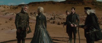Movie still from “The Tempest” (2010), directed by Julie Taymor – A group of people standing on top of a dirt field; Wide shot, Over the shoulder angle