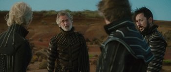 Movie still from “The Tempest” (2010), directed by Julie Taymor – A man in a black and gold jacket standing next to another man in a black jacket; Medium shot, Over the shoulder angle