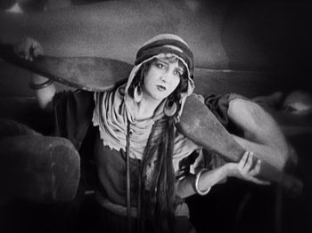 Movie still from “The Ten Commandments” (1923), directed by Cecil B. DeMille – A woman holding a large wooden object in her hands; Medium shot, High angle