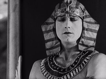 Movie still from “The Ten Commandments” (1923), directed by Cecil B. DeMille – A man wearing a pharaoh's headdress and holding his hand up to his face; Close Up shot, High angle