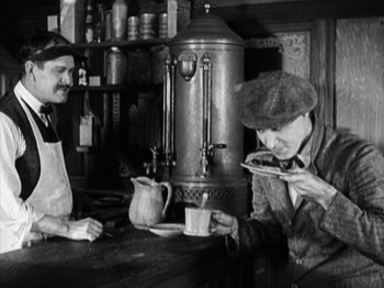 Movie still from “The Ten Commandments” (1923), directed by Cecil B. DeMille – Two men sitting at a table in front of a coffee pot; Medium shot, High angle