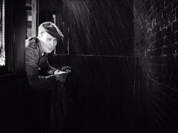 Movie still from “The Ten Commandments” (1923), directed by Cecil B. DeMille – A man standing in the rain holding a cell phone; Medium shot, High angle