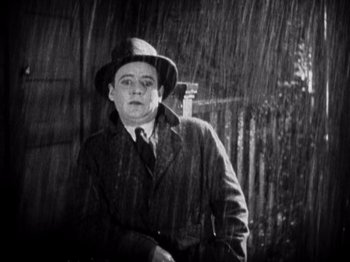 Movie still from “The Ten Commandments” (1923), directed by Cecil B. DeMille – A man wearing a hat and a coat in the pouring rain; Medium shot, Low angle
