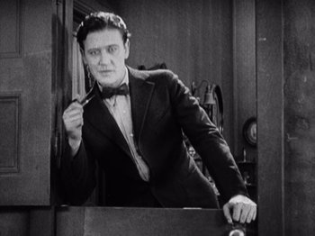 Movie still from “The Ten Commandments” (1923), directed by Cecil B. DeMille – A black and white photo of a man in a suit and bow tie; Medium shot, High angle