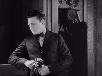 Movie still from “The Ten Commandments” (1923), directed by Cecil B. DeMille – A man in a suit and bow tie holding flowers; Medium shot, High angle