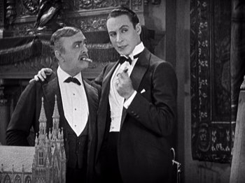 Movie still from “The Ten Commandments” (1923), directed by Cecil B. DeMille – Two men in tuxedos pose for a picture; Medium shot, Low angle