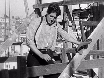 Movie still from “The Ten Commandments” (1923), directed by Cecil B. DeMille – An old black and white photo of a man working on a wooden structure; Medium shot, Low angle