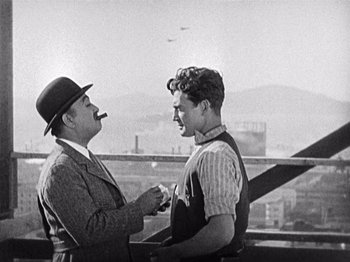 Movie still from “The Ten Commandments” (1923), directed by Cecil B. DeMille – Two men are talking on a balcony with a city in the background; Medium shot, Over the shoulder angle