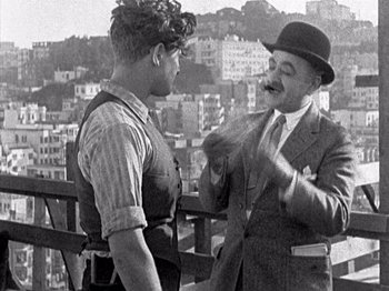 Movie still from “The Ten Commandments” (1923), directed by Cecil B. DeMille – Two men talking on a balcony with a city in the background; Medium shot, Over the shoulder angle