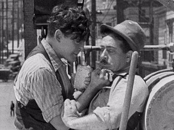 Movie still from “The Ten Commandments” (1923), directed by Cecil B. DeMille – A man and a boy eating food from a basket; Medium shot, Over the shoulder angle
