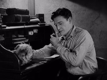 Movie still from “The Ten Commandments” (1923), directed by Cecil B. DeMille – A man sitting at a desk with a dog in front of him; Medium shot, High angle