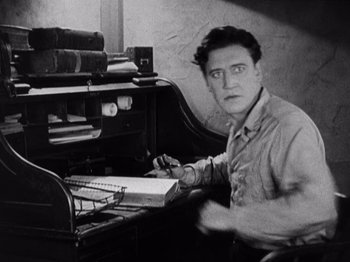 Movie still from “The Ten Commandments” (1923), directed by Cecil B. DeMille – A man sitting at a desk writing on a piece of paper; Medium shot, High angle