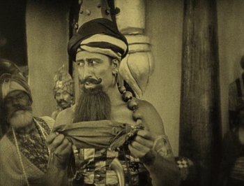 Movie still from “The Thief of Bagdad” (1924), directed by Raoul Walsh – A man with a long beard and a hat is holding something in his hands; Medium shot, High angle